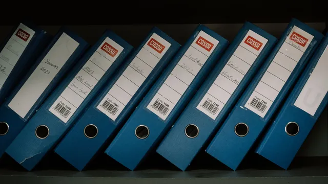 Blå ringbind med datoetiketter stillet på række i en reol