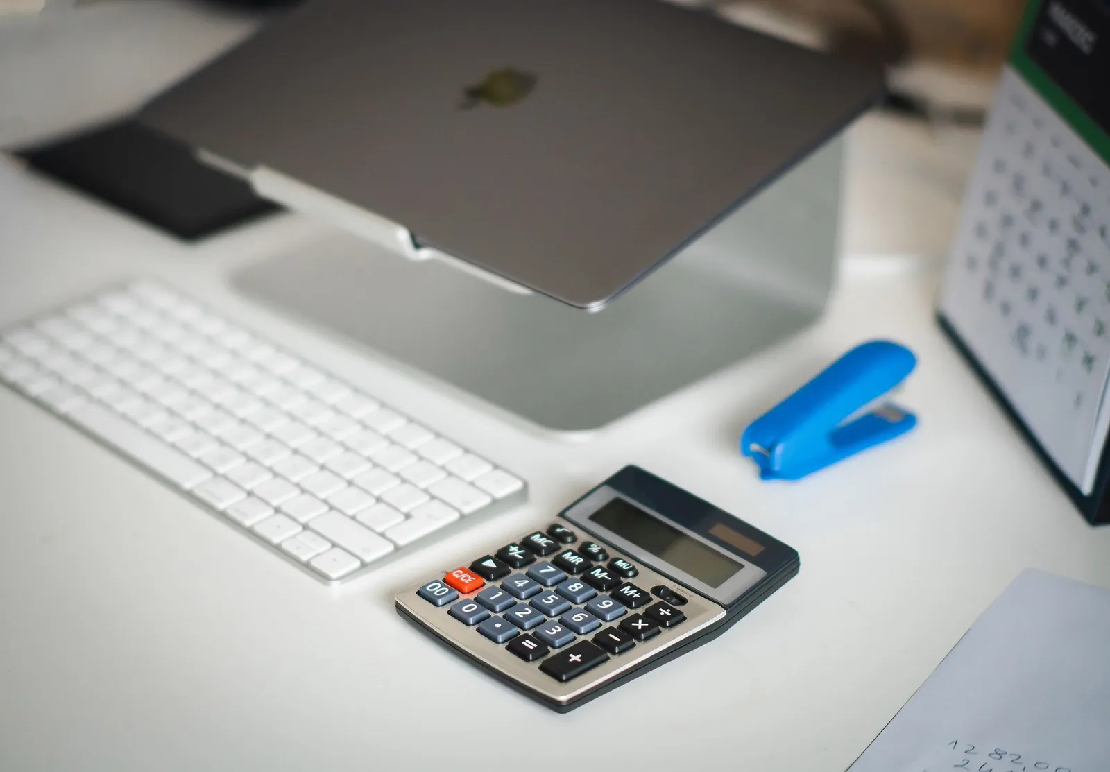 Skrivebord med bærbar computer, tastatur og regnemaskine