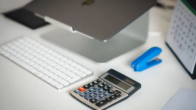 Skrivebord med bærbar computer, tastatur og regnemaskine