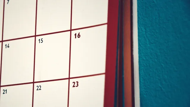 Nærbillede af en vægkalender med røde datofelter mod en blå væg