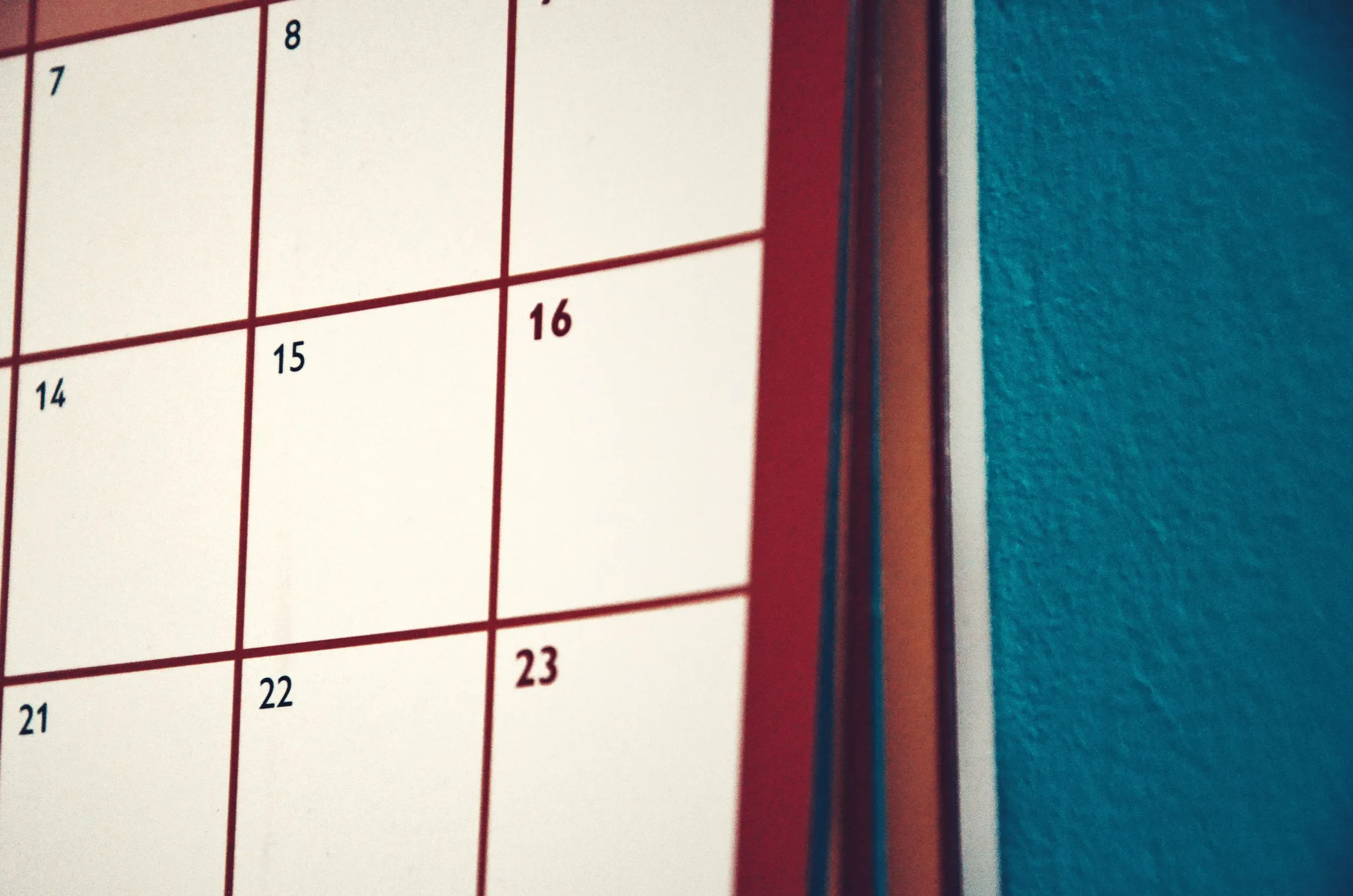 Nærbillede af en vægkalender med røde datofelter mod en blå væg