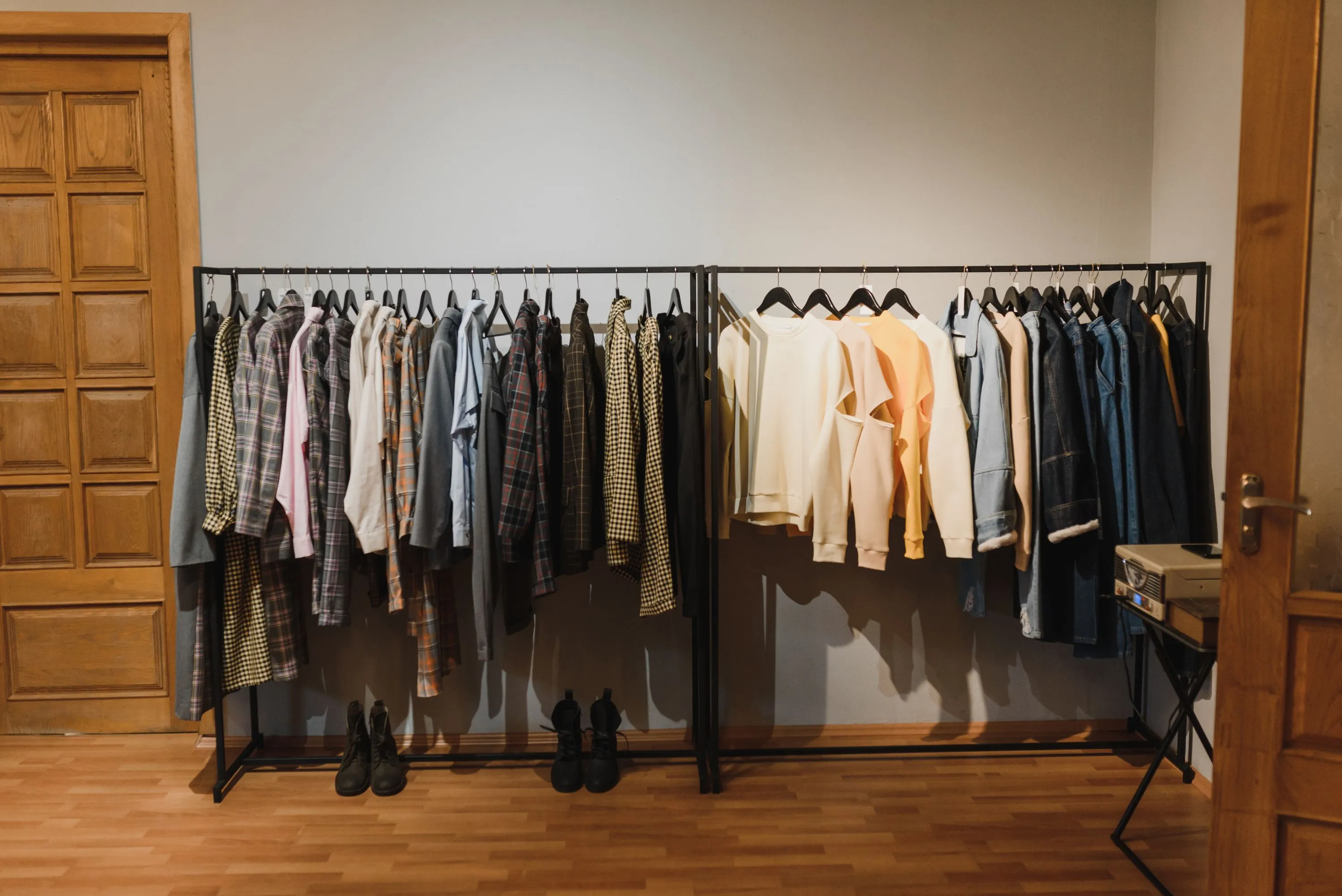 To tøjstativer med skjorter og sweatre i en butik, med støvler stillet på gulvet