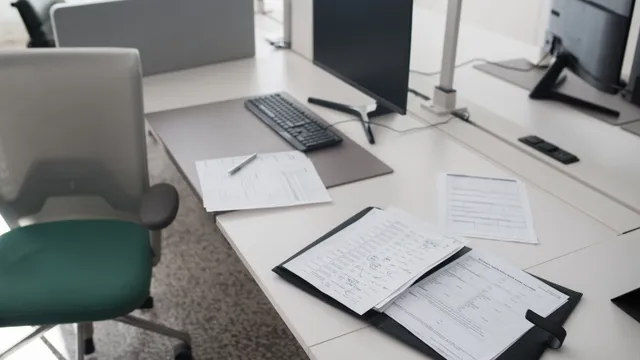 Tomt kontor med åben ringmappe, kuverter og en slukket skærm på skrivebordet