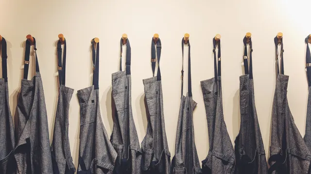 Forklæder i denim hængt på række på kroge på en væg