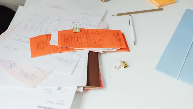 Ryddeligt skrivebord med kvitteringer, fakturaer og kontorartikler
