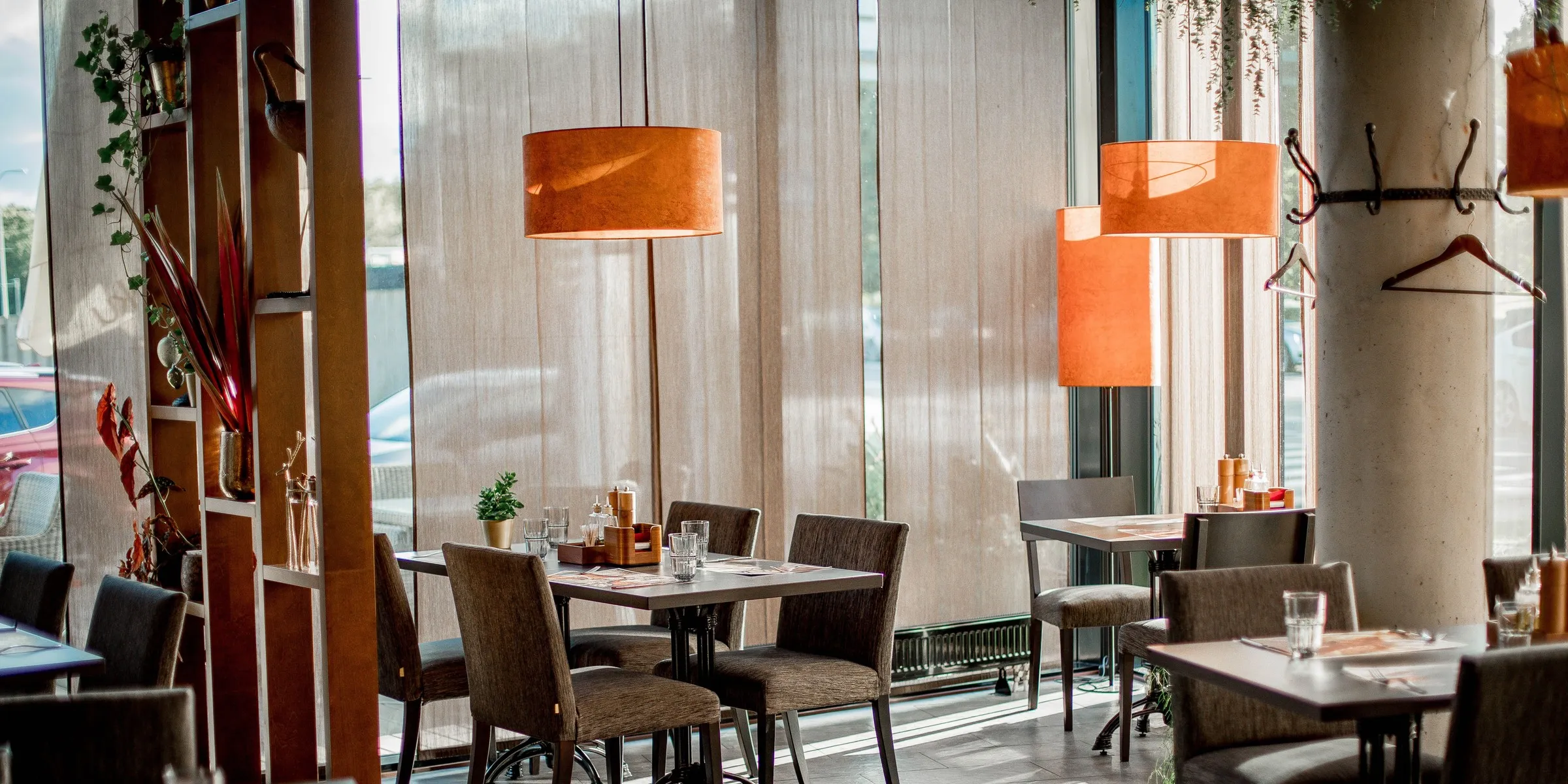 Tomt restaurantlokale med borde dækket op under varmt lys fra pendellamper