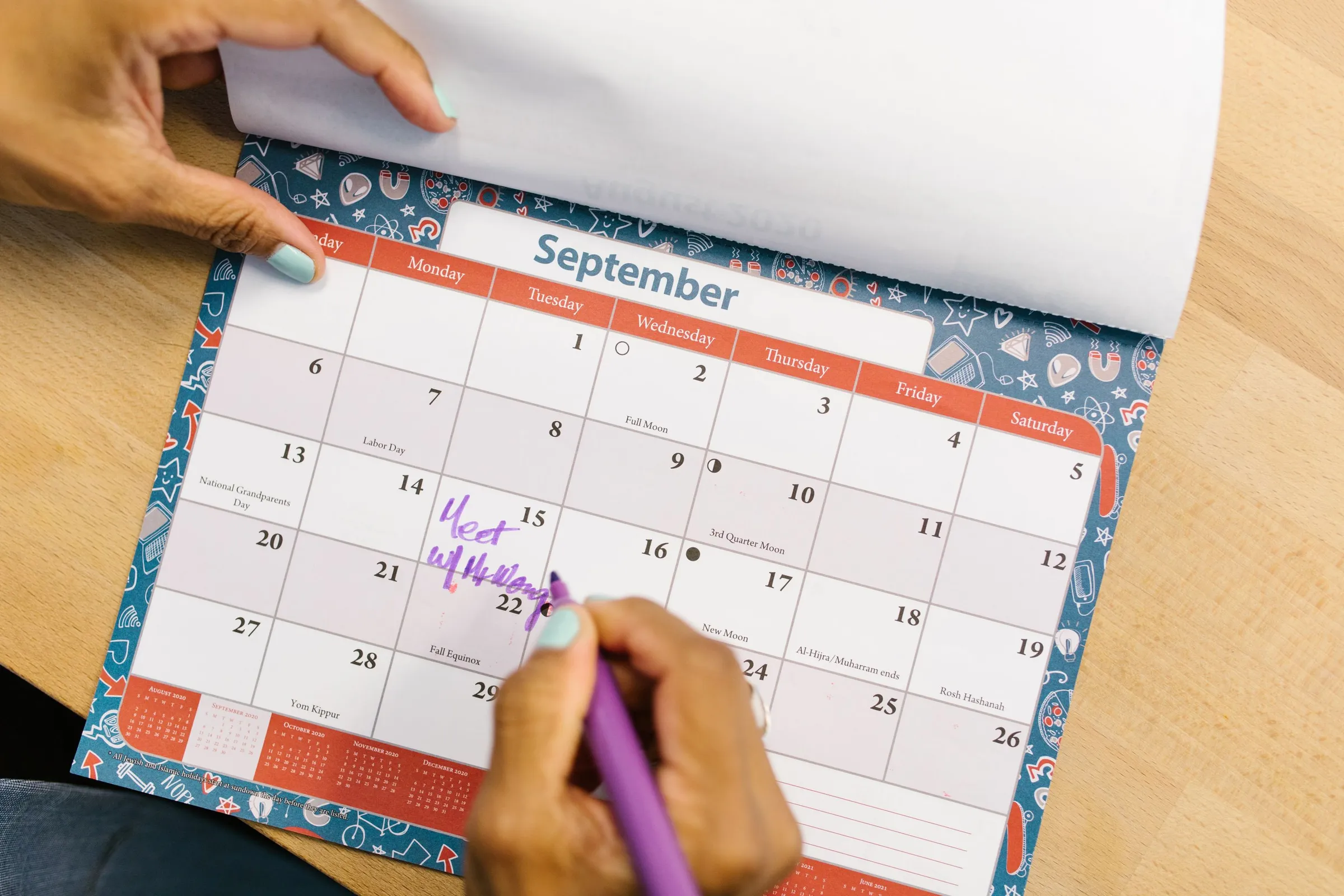 Hånd der markerer en dato i september i en bordkalender på et skrivebord