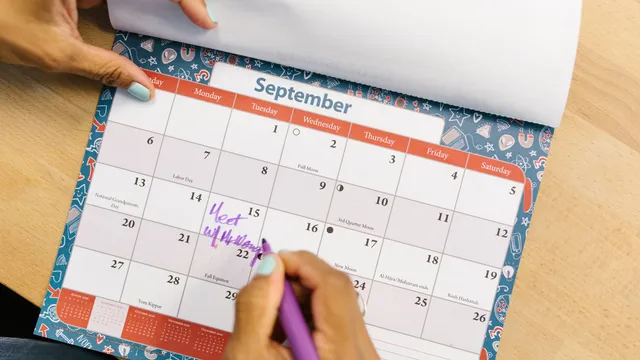 Hånd der markerer en dato i september i en bordkalender på et skrivebord